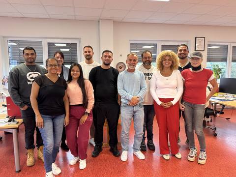 Das Pflegeteam von CuraSol im Büro, rund ein Dutzend Pflegekräfte stehen nebeneinander und lächeln